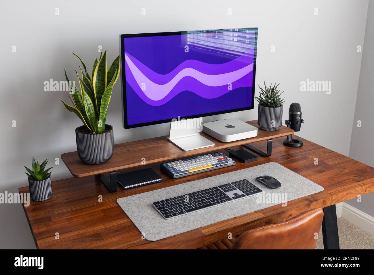 LONDRA - 24 AGOSTO 2023: Apple Studio display e Mac Mini computer in un moderno ufficio domestico, lavoro da casa configurazione minima della scrivania sfondo viola Foto Stock