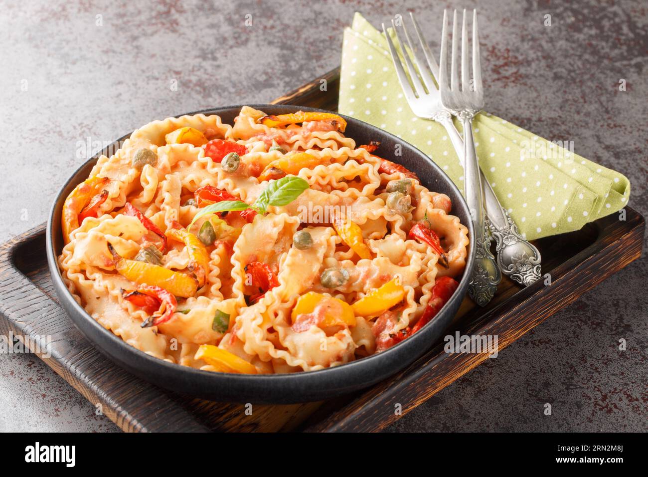 Reginette con peperoni e basilico in salsa di pomodoro cremosa con primi piani di capperi sul piatto sul tavolo. Orizzontale Foto Stock