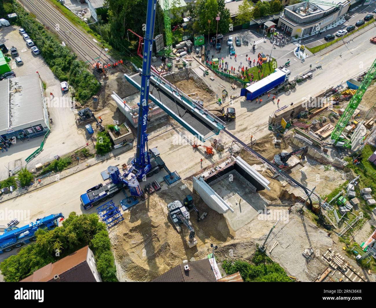 Starnberg, Germania. 31 agosto 2023. Una gru solleva un nuovo cavalcavia ferroviario sull'autostrada federale 2 a Starnberg fino alla sua fondazione. (Foto aerea scattata con un drone) il nuovo ponte avrà un'altezza di 4,5 metri e una larghezza di 26,3 metri. Due sovrastrutture in acciaio, ognuna del peso di 120 tonnellate, sono state sollevate nella loro posizione finale da una gru blu montata su autocarro da 650 tonnellate. Crediti: Peter Kneffel/dpa/Alamy Live News Foto Stock