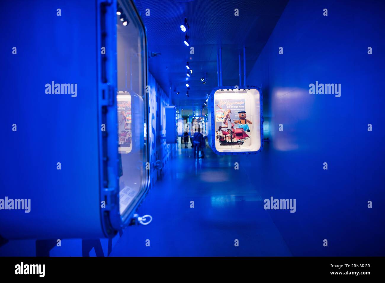 M/S Maritime Museum of Denmark Gallery Corridor Helsingor // HELSINGOR, Danimarca — Un corridoio galleria illuminato in blu presso il M/S Maritime Museum of Denmark presenta vetrine incassate che mostrano manufatti e giocattoli marittimi. L'innovativo design espositivo fa parte della ristrutturazione del museo del 2013 all'interno di un ex bacino di carenaggio. Il museo, situato accanto al castello di Kronborg, presenta il patrimonio marittimo della Danimarca attraverso approcci architettonici e curatoriali contemporanei. Foto Stock