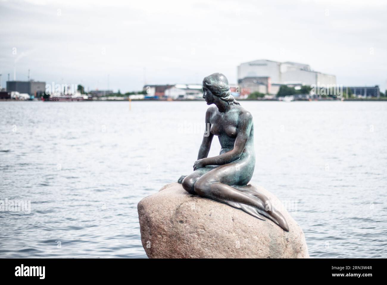 La statua della Piccola Sirena Copenaghen Danimarca | COPENHAGEN, Danimarca — La Piccola Sirena in bronzo è appollaiata su un masso di granito sul lungomare di Langelinie Promenade, dove è seduta dalla sua installazione il 23 agosto 1913. Sculptata da Edvard Eriksen e commissionata nel 1909 da Carl Jacobsen come regalo alla città, la figura è ispirata alla fiaba omonima di Hans Christian Andersen del 1837. La combinazione di bronzo fuso e del masso di granito naturale sottostante ha reso la composizione una delle scene più riconoscibili e frequentemente fotografate di Copenaghen. Foto Stock