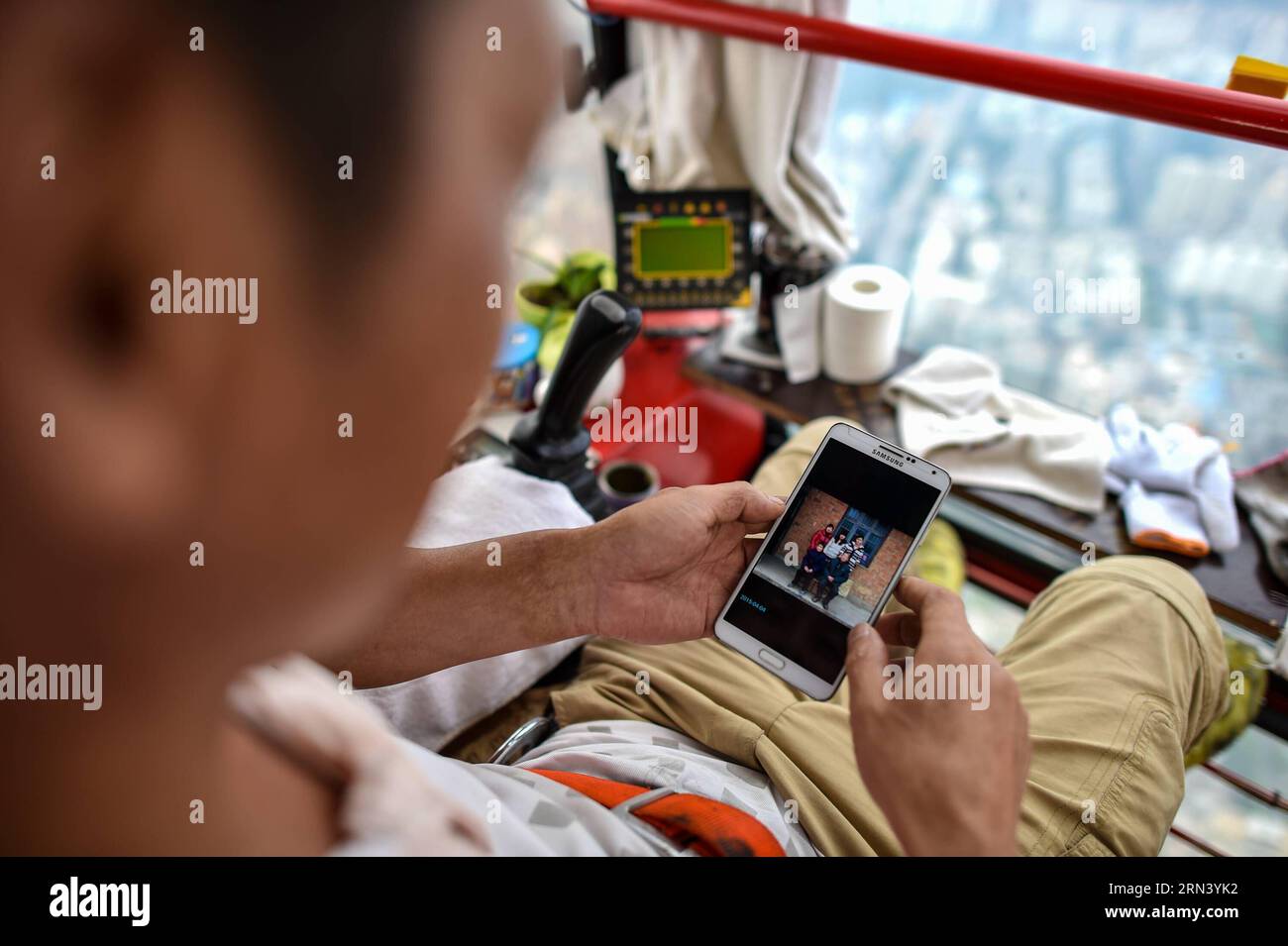 (150430) -- SHENZHEN, 30 aprile 2015 -- foto scattata il 18 aprile 2015 mostra Wang Hua, un operatore di gru a torre, guarda una foto della sua famiglia sul suo cellulare mentre riposa su una gru a torre a Shenzhen, nella provincia del Guangdong nel sud della Cina. Wang Hua, 50 anni della provincia di Henan, è una buona persona nella gru a torre operativa. Anche se era una guardia di sicurezza quando era giovane, è diventato rapidamente un eccellente operatore di gru a torre grazie alla sua diligenza e al suo amore per l'apprendimento. Fu impegnato in molti progetti di costruzione più grandi come il nuovo sito di CCTV e il Water Cube, e il Foto Stock