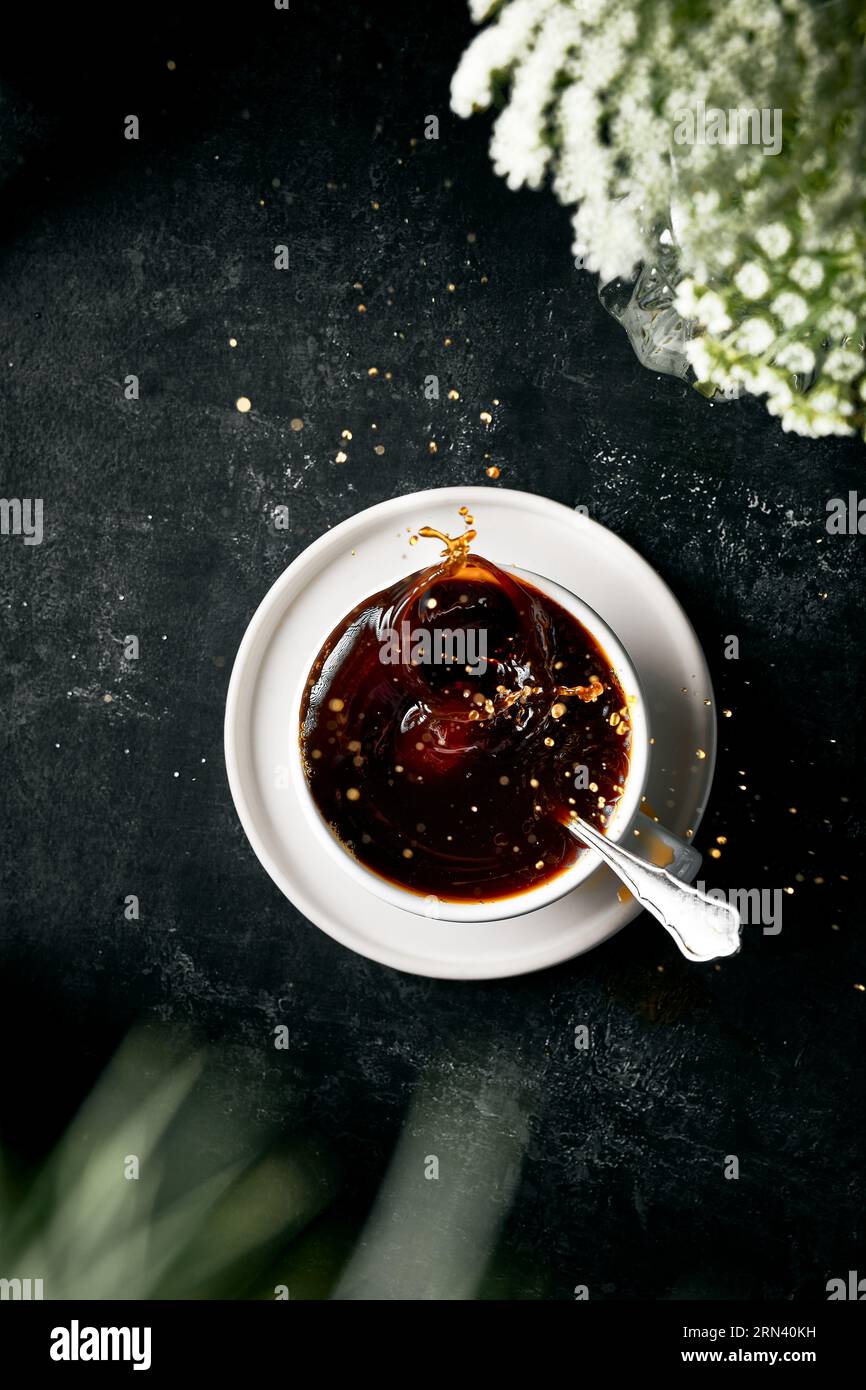 Vista dall'alto immagine verticale di schizzi nella tazza di caffè. Caffè nero nella tazza bianca. Sfondo nero scuro testurizzato. Foto Stock