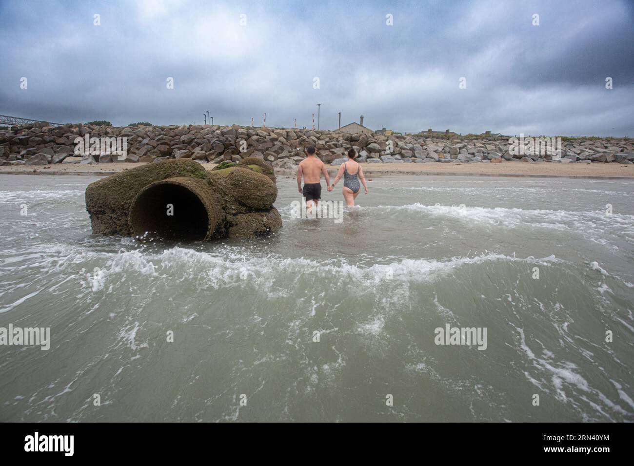 Nuotatore che cammina fuori dal mare accanto al tubo di deflusso alla spiaggia di Longrock tra Penzance e Marazion in Cornovaglia , Regno Unito. Foto Stock