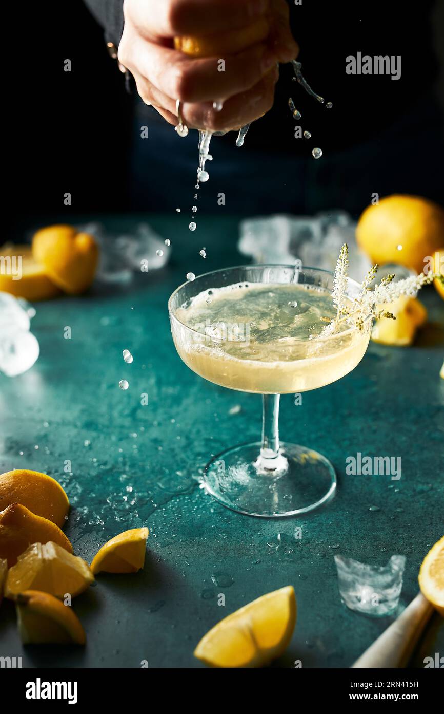 Spremere a mano il succo di limone in un bicchiere di cocktail giallo schiumoso trasparente. Molti limoni. Moody Still Life. Bevanda rinfrescante. Foto Stock