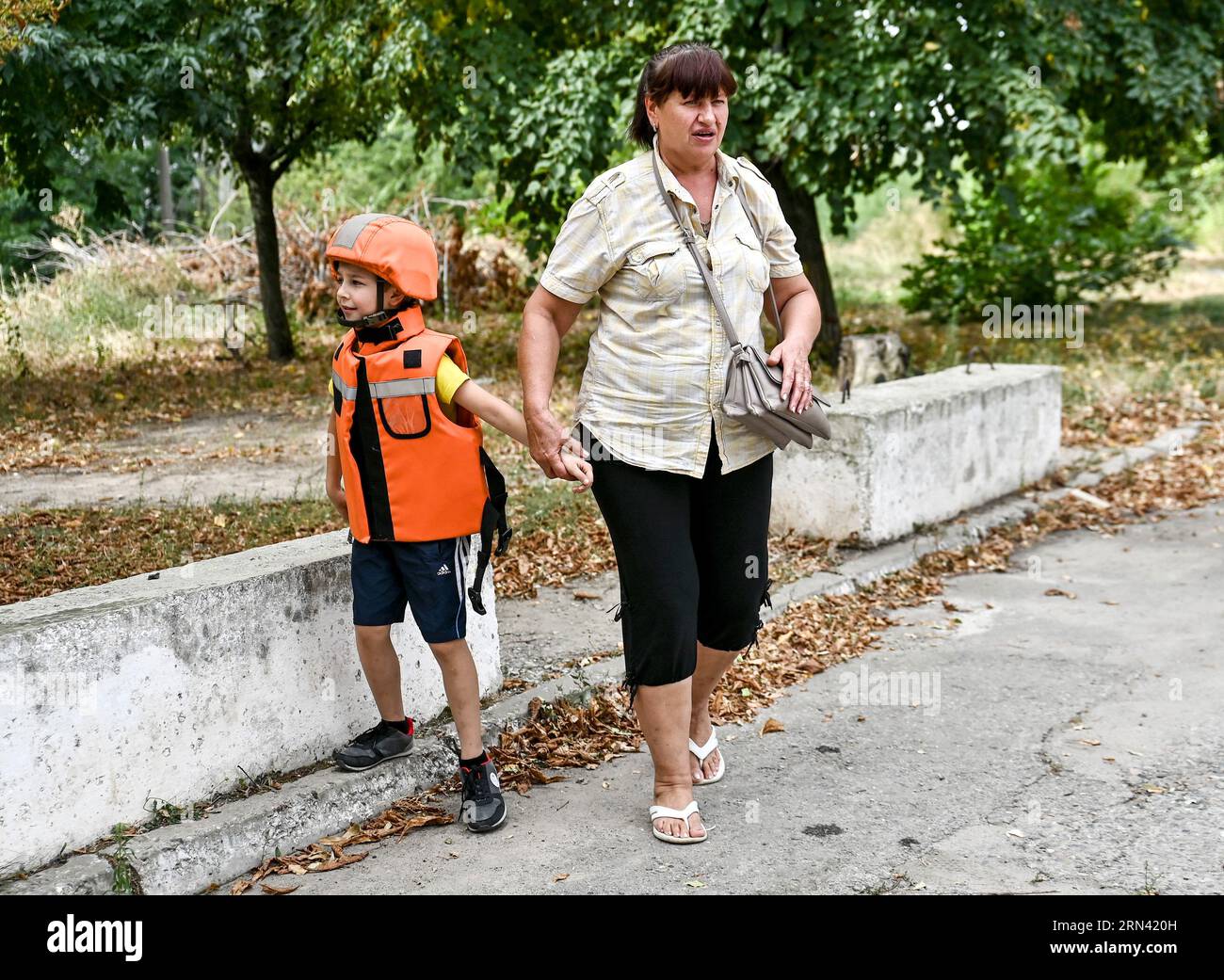 Non esclusiva: ZAPORIZHZHIA, UCRAINA - 31 AGOSTO 2023 - Una donna anziana tiene a mano un ragazzo in un casco e un giubbotto di salvataggio dopo che due famiglie sono state Foto Stock