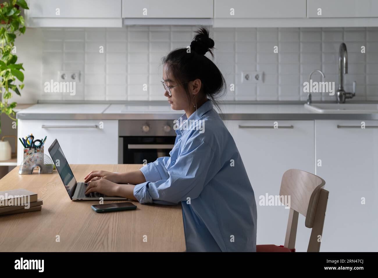 Focalizzato giovane asiatica freelance blogger lavorare su laptop in cucina Foto Stock