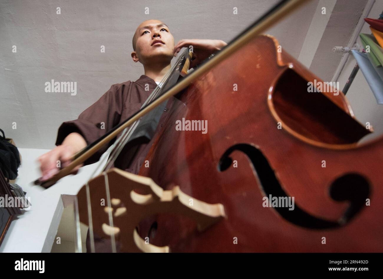 Un monaco suona il violoncello nel tempio di Tiantai nella contea di Hong an, nella provincia di Hubei, nella Cina centrale, l'8 maggio 2015. I monaci del Tempio di Tiantai sono competenti non solo nel dharma del Buddha, ma anche negli strumenti orchestrali. Il Maestro Wule ha iniziato a ricostruire il Tempio di Tiantai, vecchio di 1400 anni, dal 2004. Come ex musicista, organizzò l'orchestra monaca Guangxuan per predicare il buddhismo e la filosofia Zen attraverso la musica nel 2008. I membri dell'orchestra imparano a suonare strumenti da zero e a superare numerose difficoltà. Attirando credenti e monaci che si identificano con l'idea della pratica buddhista Foto Stock