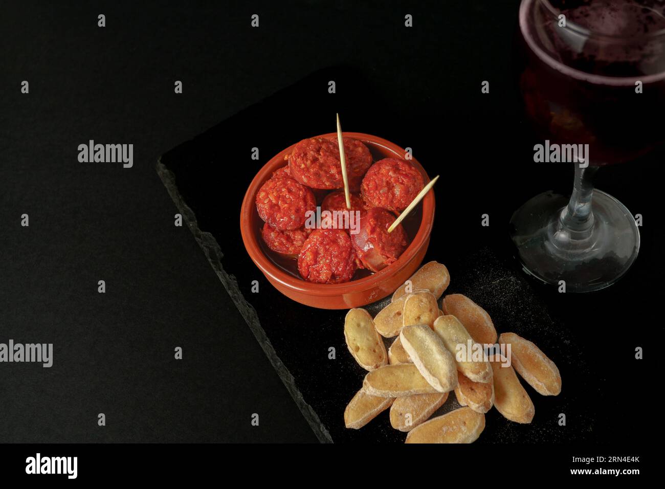 Chorizo iberico, salsiccia iberica, fritta in vaso di argilla con pane e vino rosso tipico tapa spagnolo isolato su fondo nero e spazio copia Foto Stock