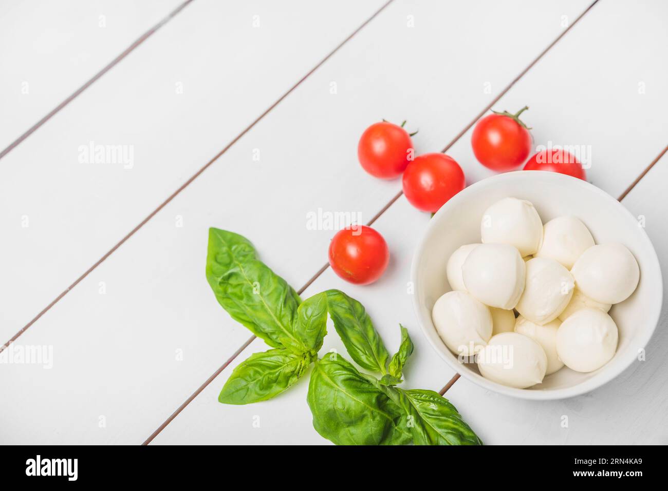 Palla di mozzarella con foglia di basilico pomodori rossi fondo bianco in legno Foto Stock