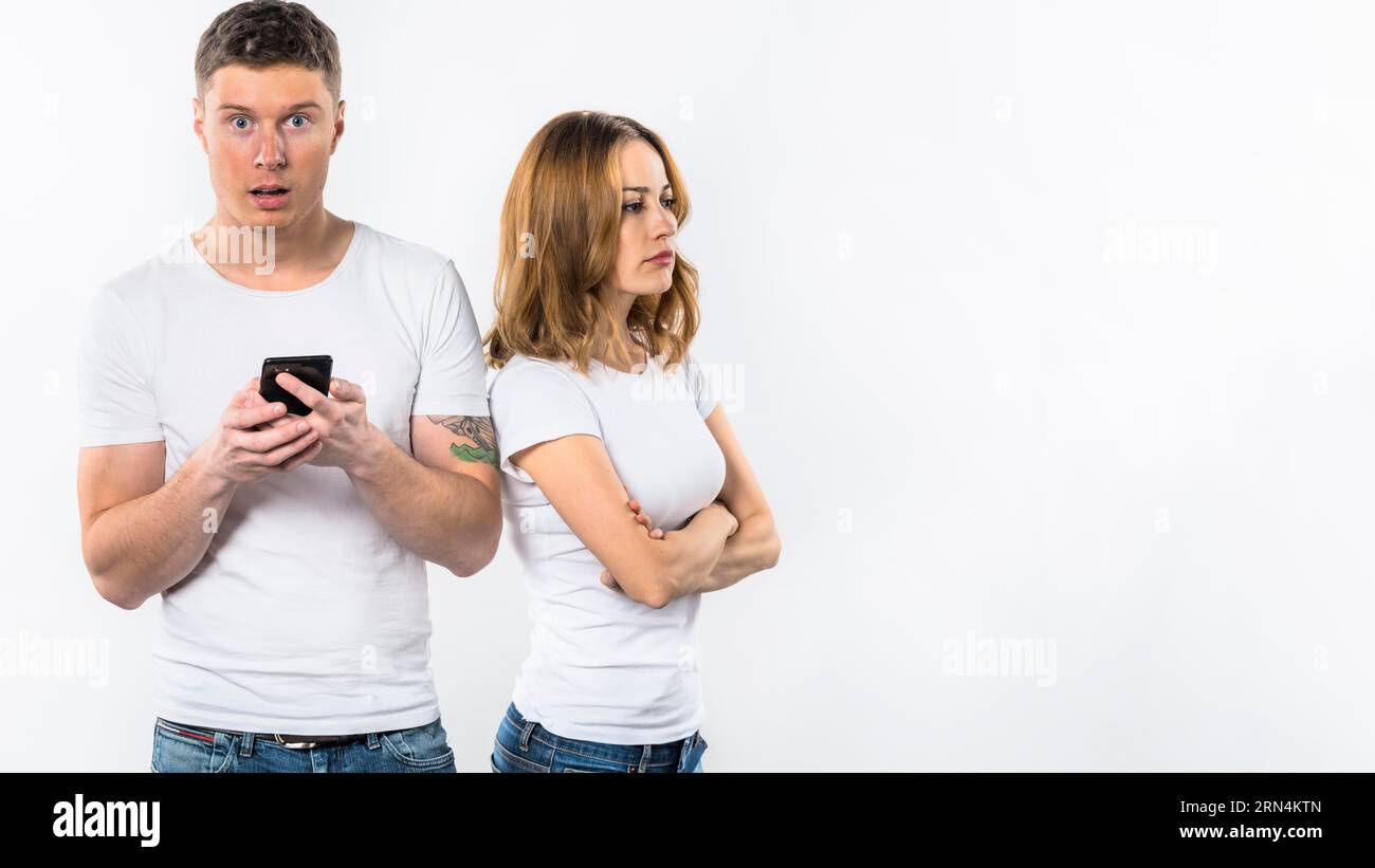Un uomo scioccato che tiene la mano del telefono cellulare in piedi vicino alla sua ragazza arrabbiata Foto Stock