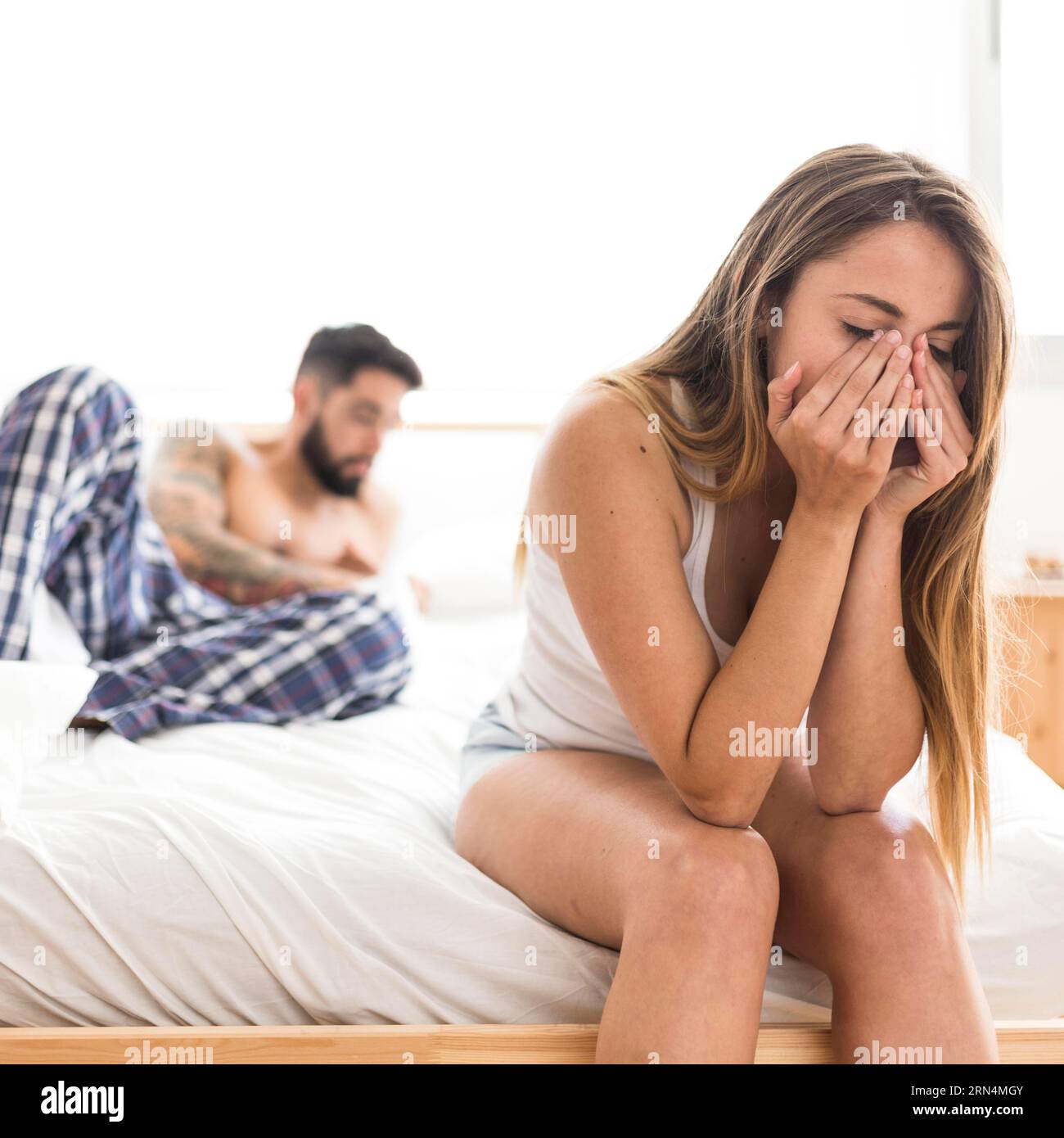 Donna turbata seduta letto davanti suo marito Foto Stock