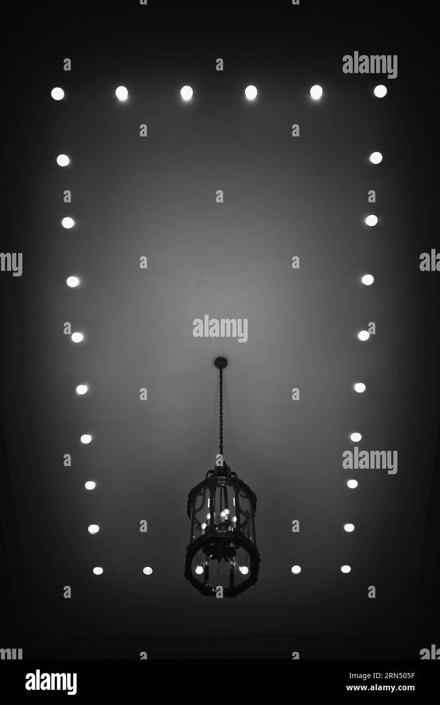 Lampadario e plafoniere. Fotografia in bianco e nero di un lampadario sospeso circondato da una griglia di luci da incasso nel soffitto. Foto Stock