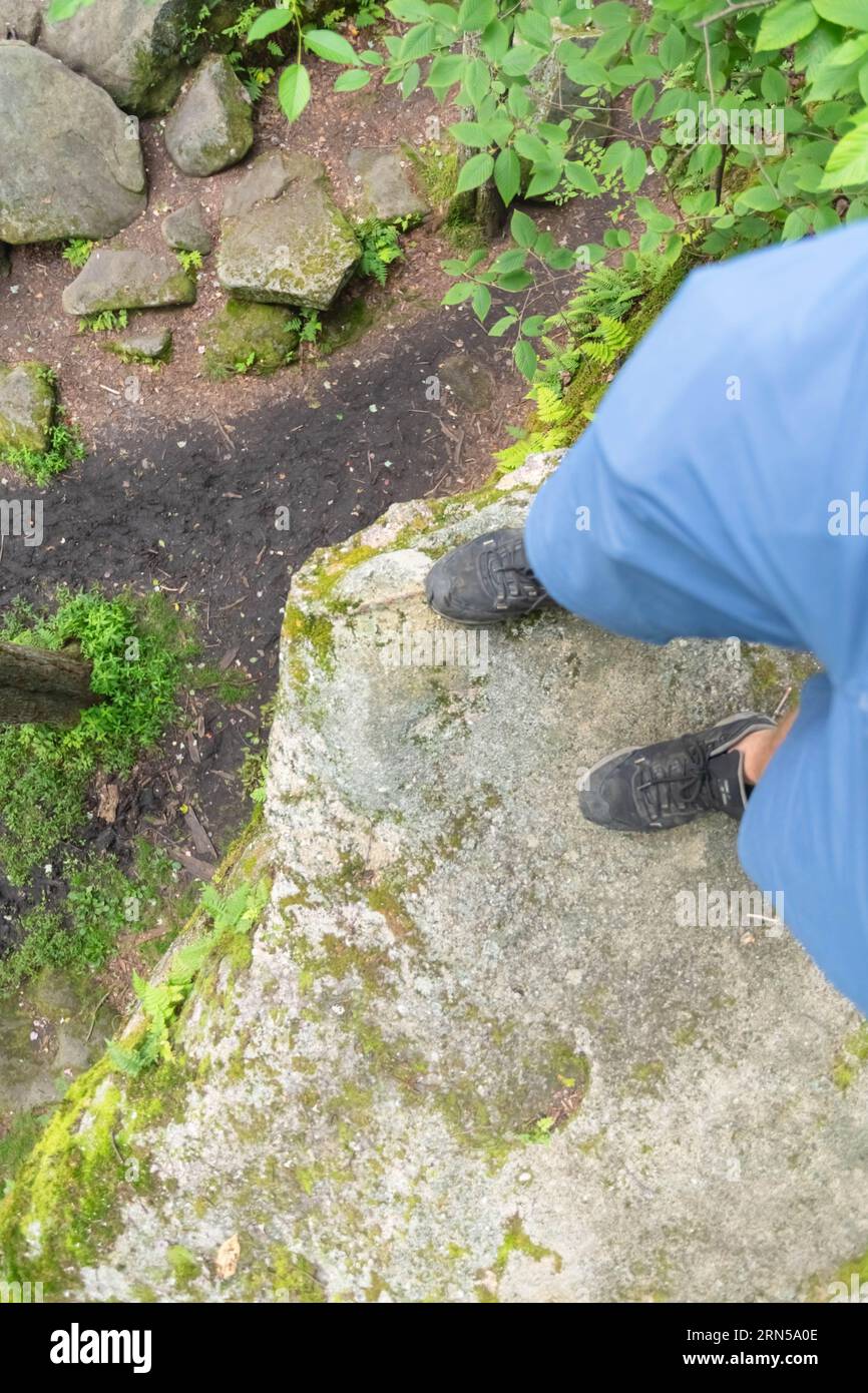 Escursionista che guarda in basso da un bordo di un masso di pietra Foto Stock