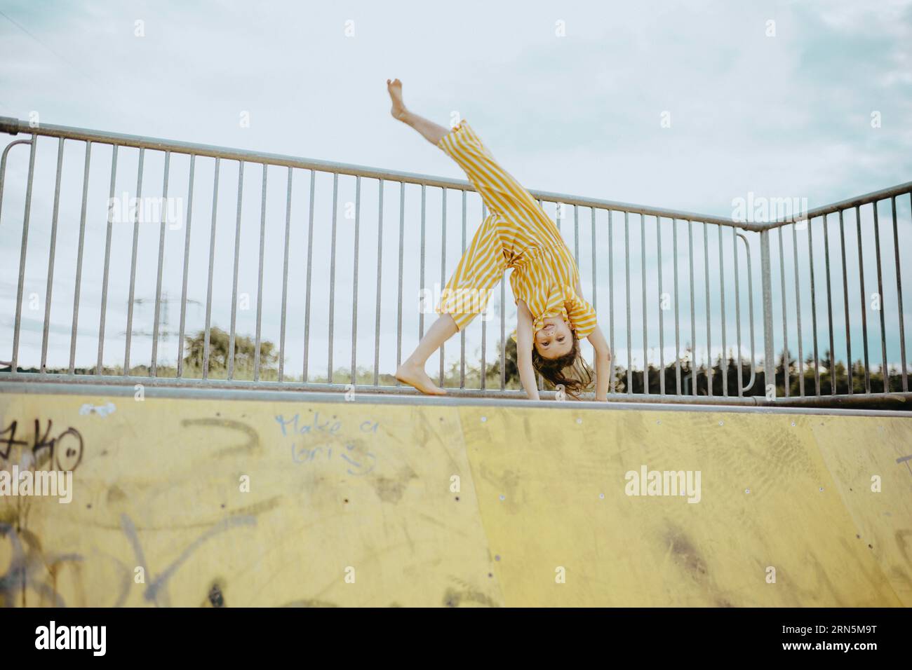 Ragazza, 9 anni, in tuta a a righe gialle e bianche fa un cartwheel, moda Foto Stock