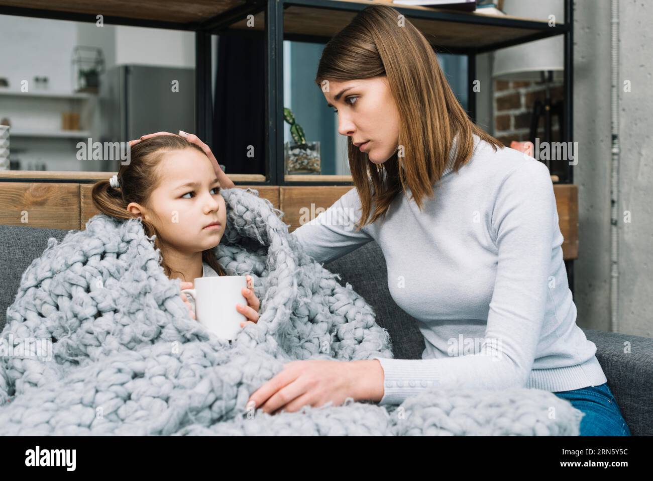 Madre che si prende cura di sua figlia coperta di sciarpa di lana grigia che soffre di febbre Foto Stock