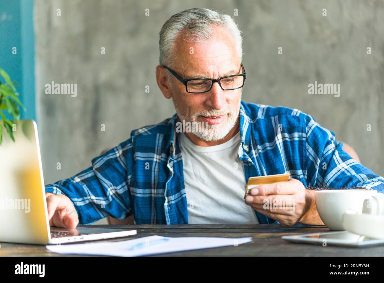 Uomo anziano che legge il numero di carta di credito mentre lavora con un computer portatile Foto Stock