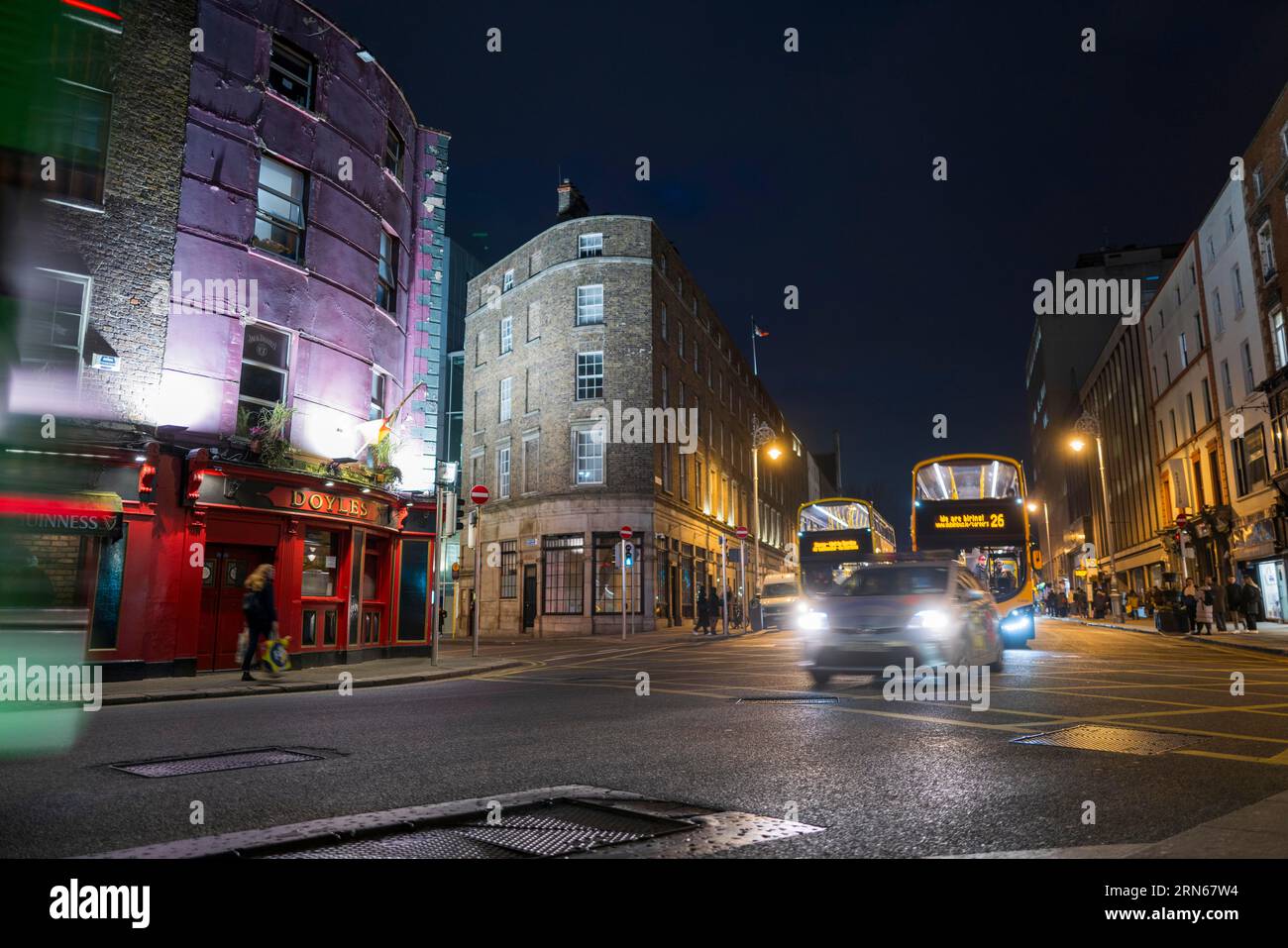 Un'auto e gli autobus di Dublino passano davanti al pub Doyle's e proseguono verso il Trinity College di notte. Dublino, Irlanda Foto Stock