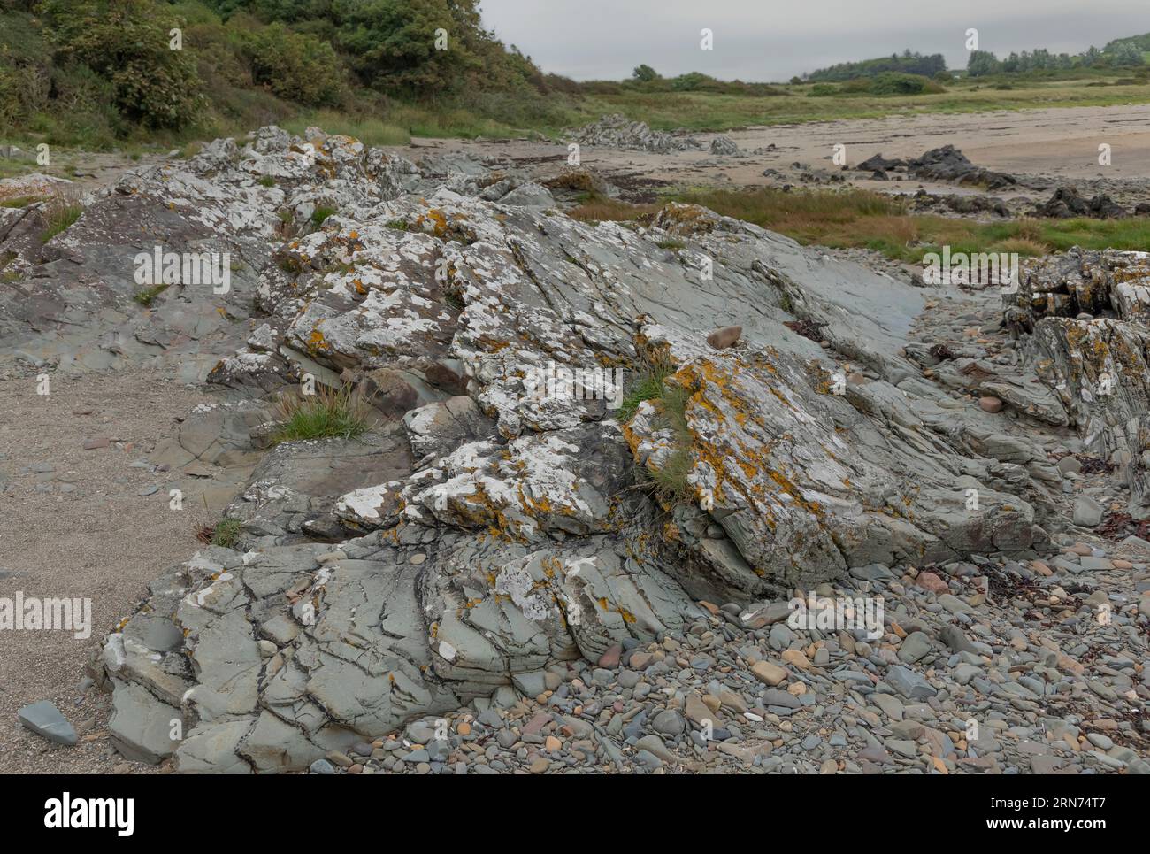 Le rocce rocciose ricoperte di licheni rocciosi si estendono dalla sabbia grossolana Foto Stock