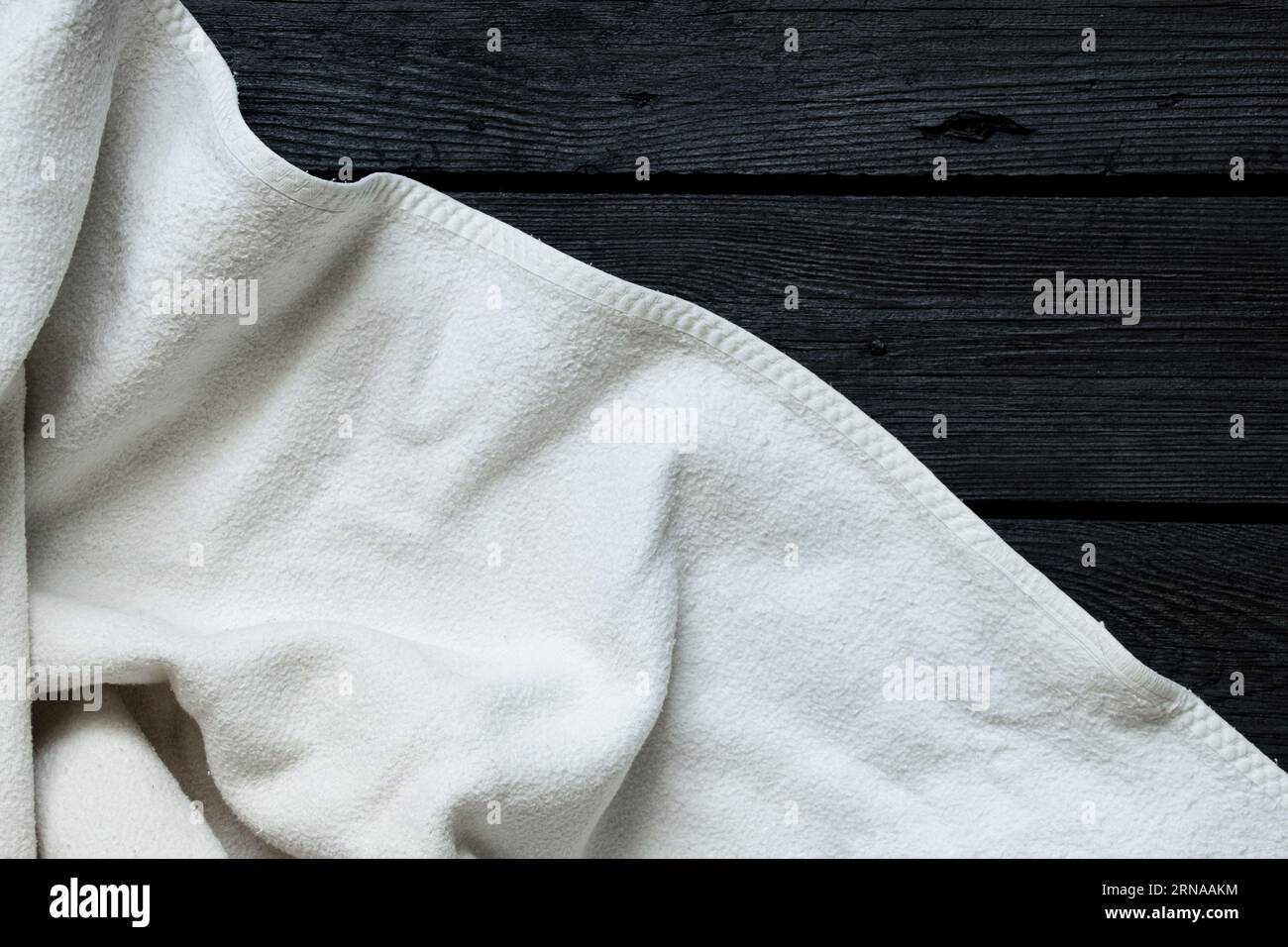 Un tessuto bianco e morbido si trova su una tavola di legno nero come sfondo, un luogo per il testo, uno sfondo bianco-nero, una coperta giace sul pavimento della casa Foto Stock