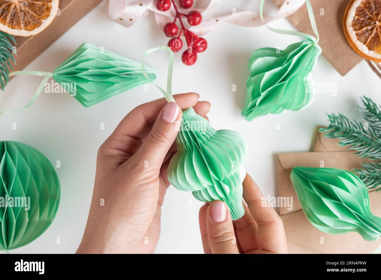 Le mani femminili aprono gli ornamenti di carta natalizi a nido d'ape. Decorazioni in plastica pieghevoli fatte a mano. Concetto di artigianato invernale. Eco-DIY alla moda. SC Foto Stock