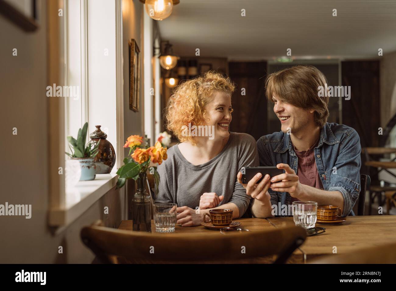 Coppia felice che usa lo smartphone mentre si siede al tavolo con un caffè Foto Stock