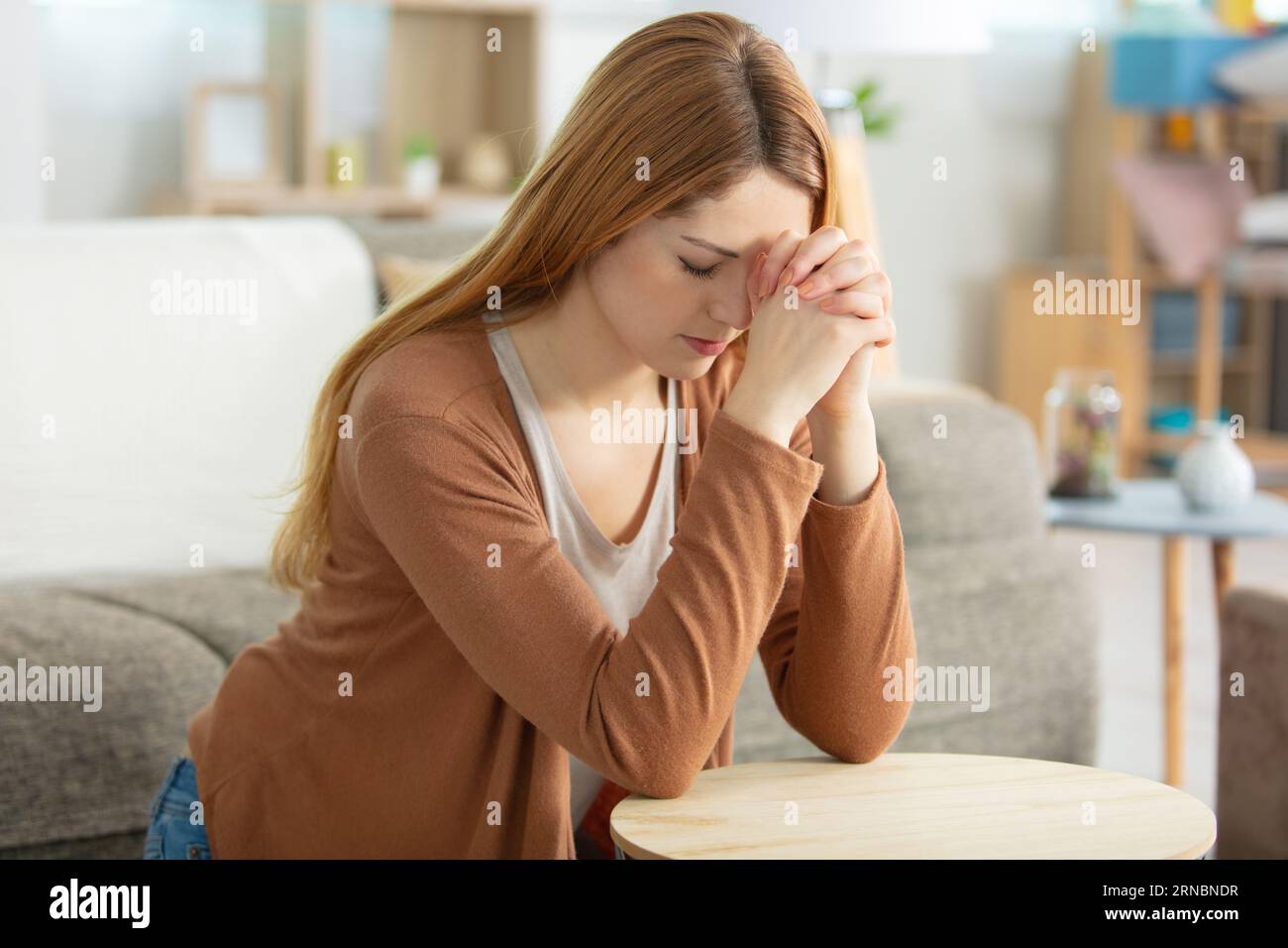 donna inginocchiata in preghiera nel soggiorno Foto Stock