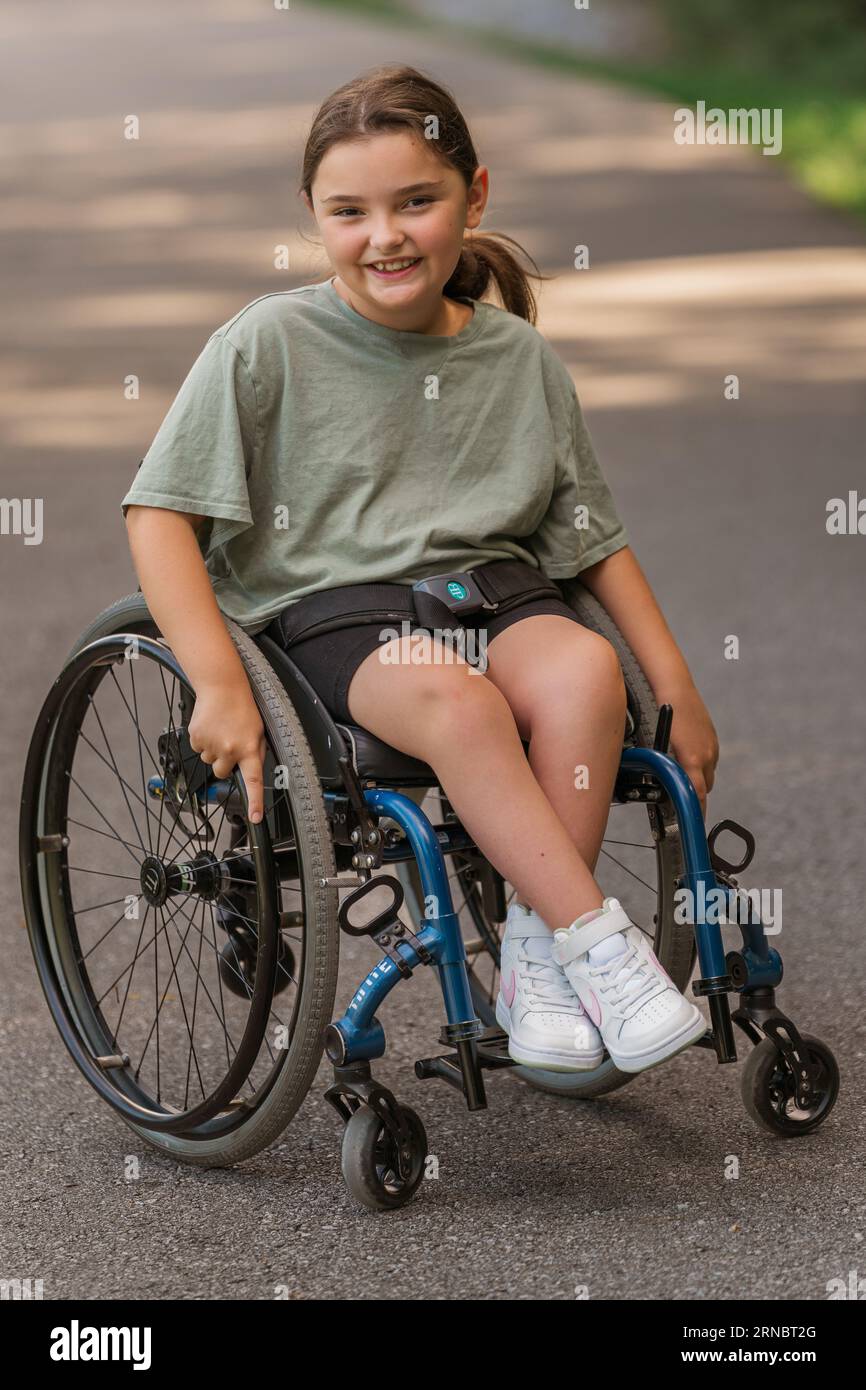 Una ragazza sorridente mentre è seduta su una sedia a rotelle al parco Foto Stock