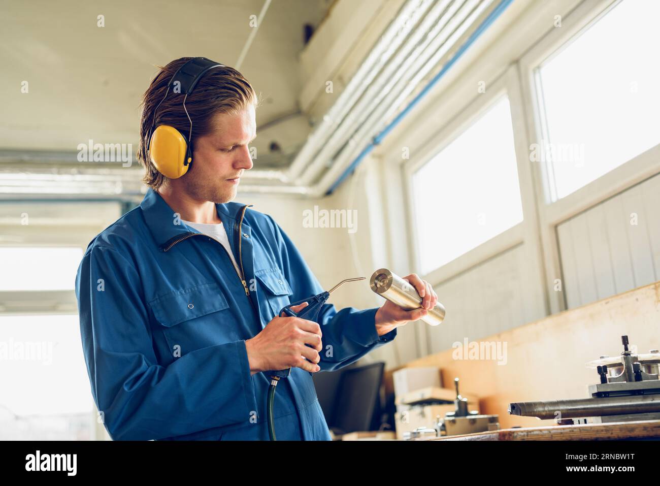 Giovane uomo concentrato con cuffie in piedi con gli strumenti in fabbrica Foto Stock