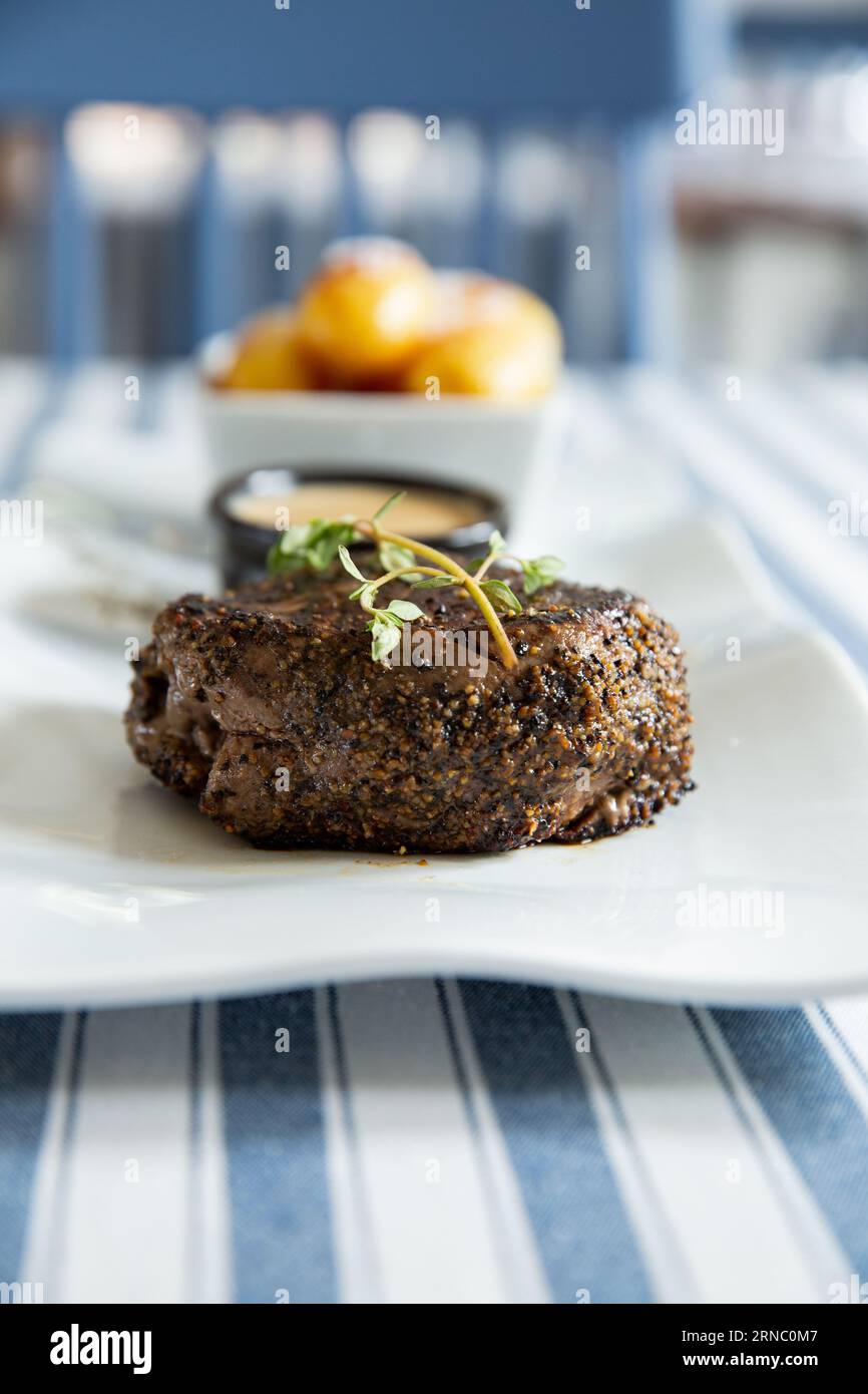 Stuzzicante bistecca di manzo alla griglia media con patate al forno e salsa servita su piatto bianco. Foto Stock