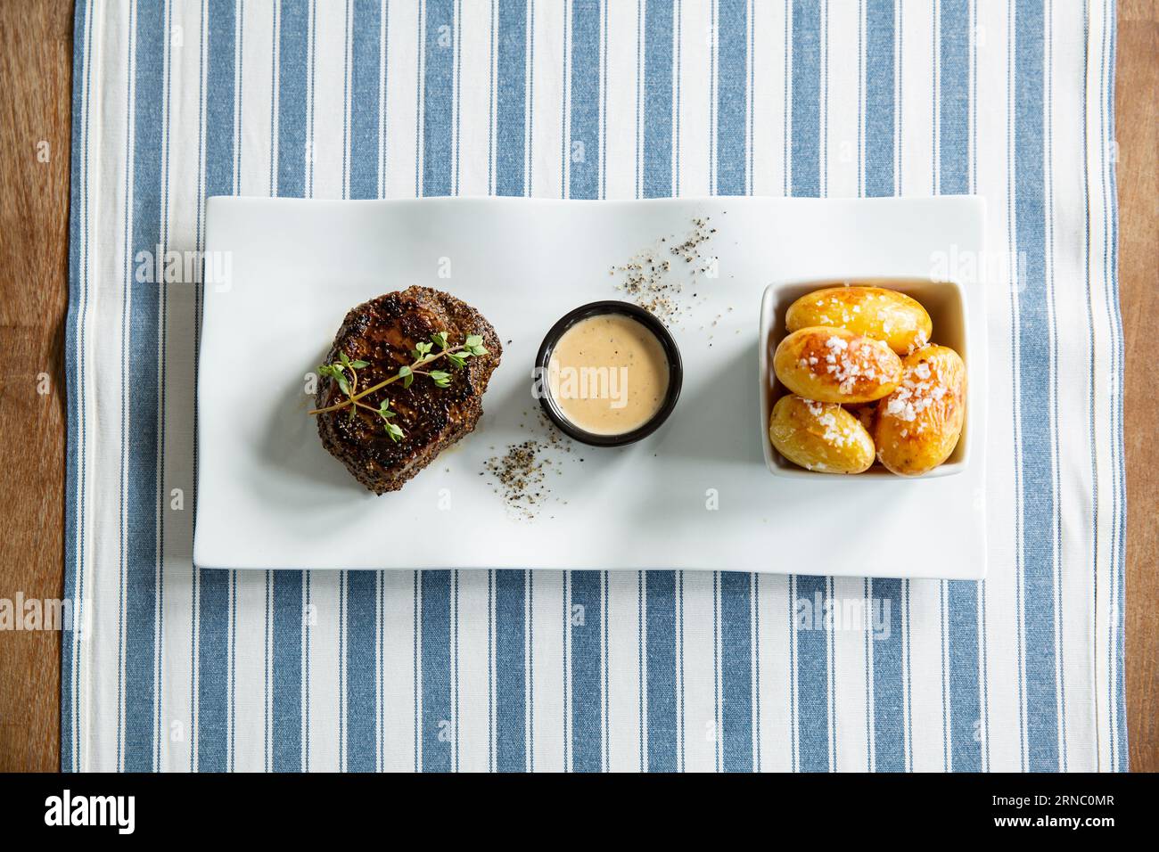 Stuzzicante bistecca di manzo alla griglia media con patate al forno e salsa servita su piatto bianco. Foto Stock
