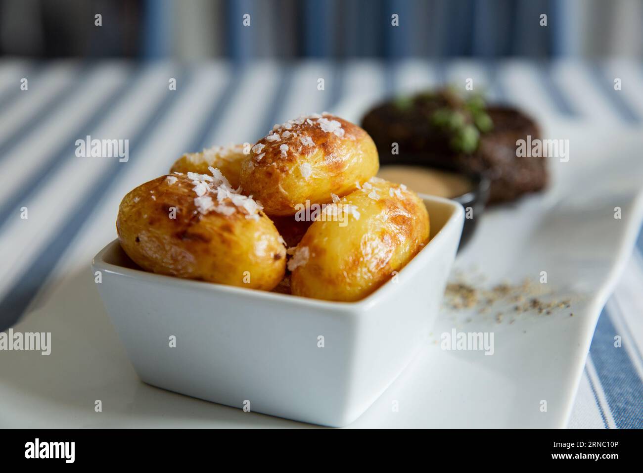 Stuzzicante bistecca di manzo alla griglia media con patate al forno e salsa servita su piatto bianco. Foto Stock