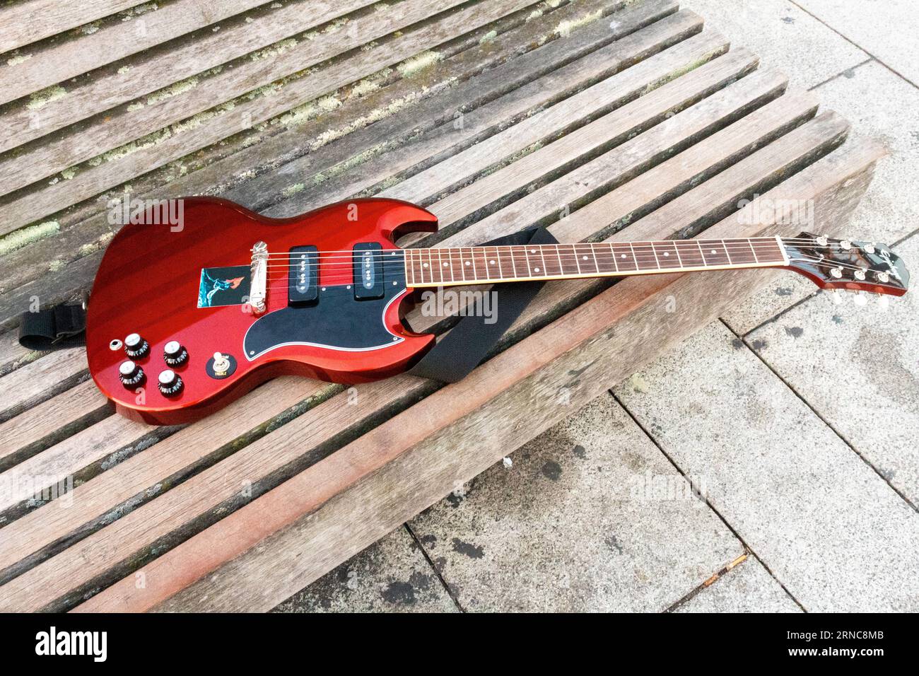 Una chitarra elettronica rossa è stata lasciata in cima a una panchina di legno. Foto grandangolare di alta qualità Foto Stock