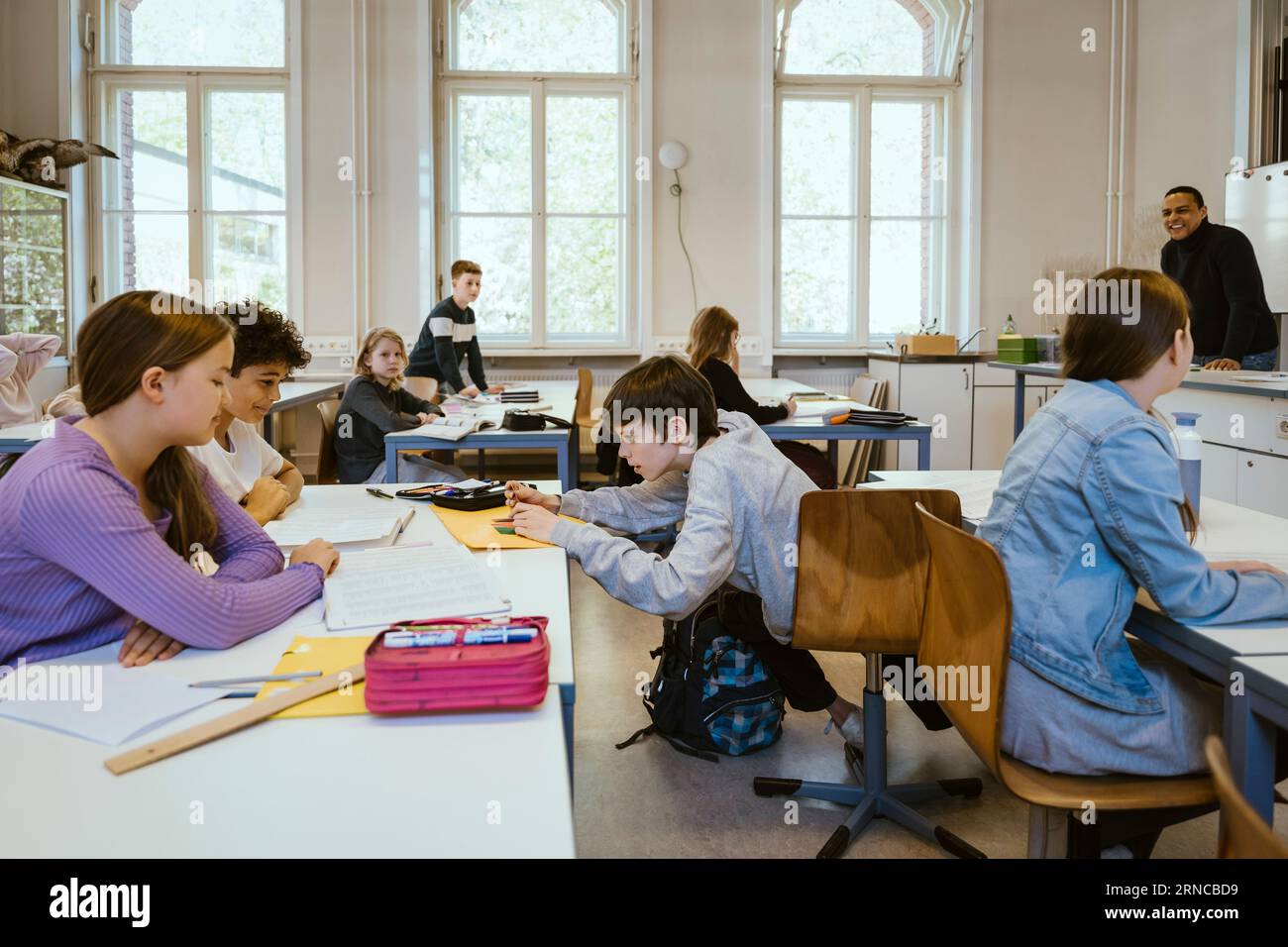 Scolaro che assiste gli amici seduti sulla scrivania in classe Foto Stock