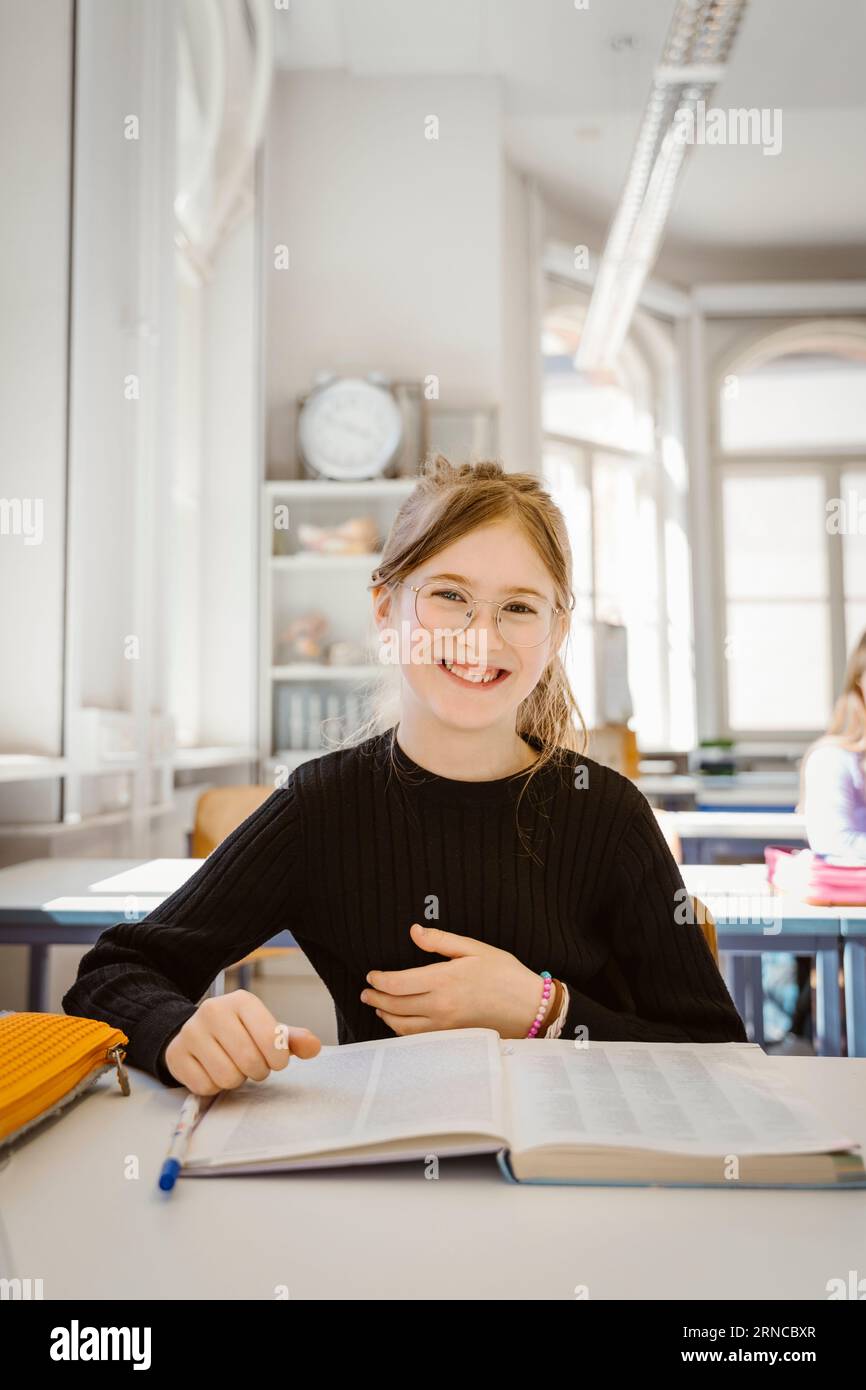 Ritratto di una studentessa felice con un libro alla scrivania in classe Foto Stock