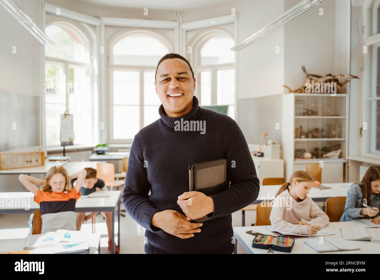 Ritratto di un insegnante maschio sorridente che tiene in mano un tablet PC mentre si trova in classe Foto Stock