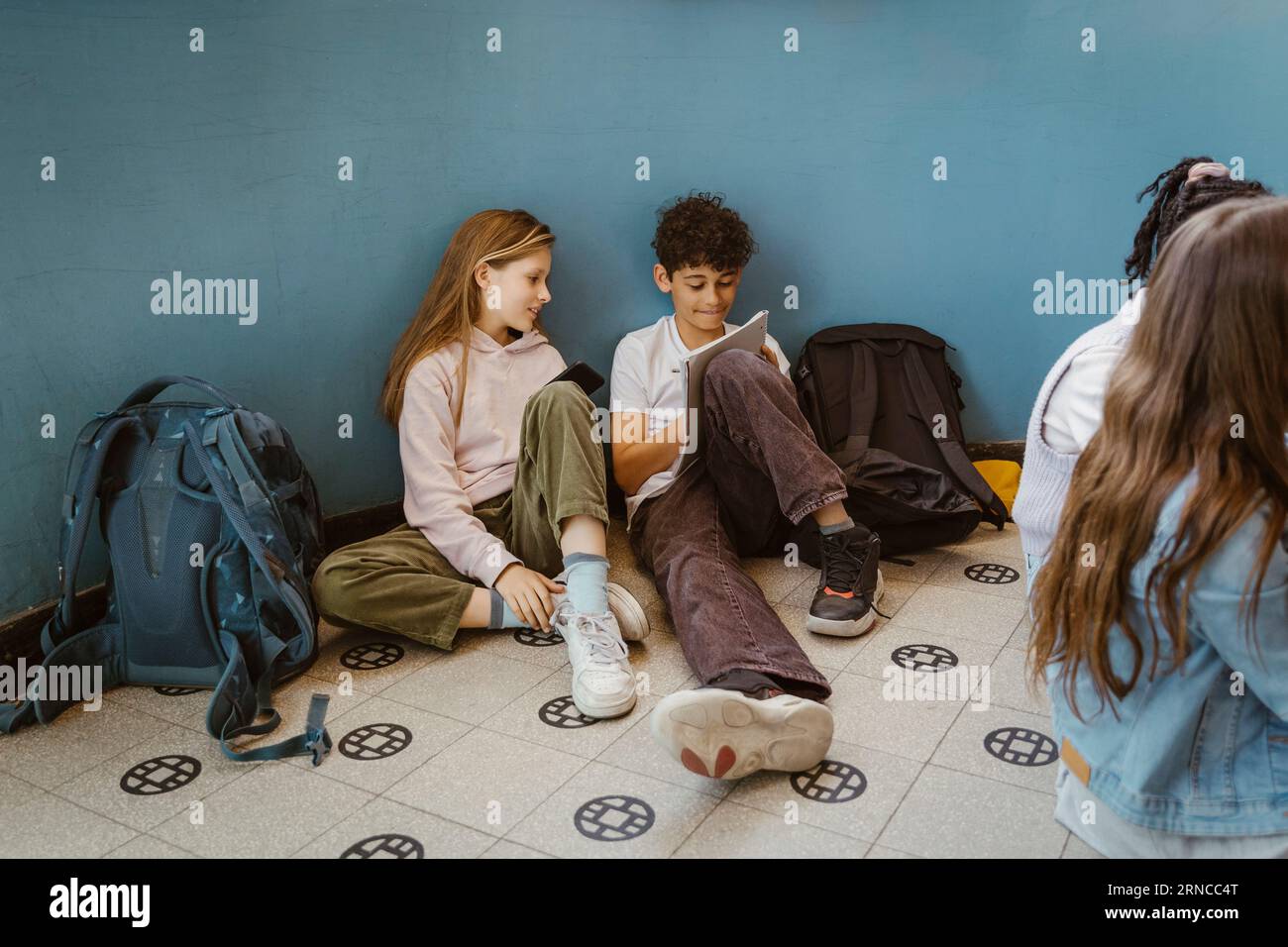 Ragazzo e ragazza che studiano insieme mentre sono seduti vicino al muro nell'edificio scolastico Foto Stock