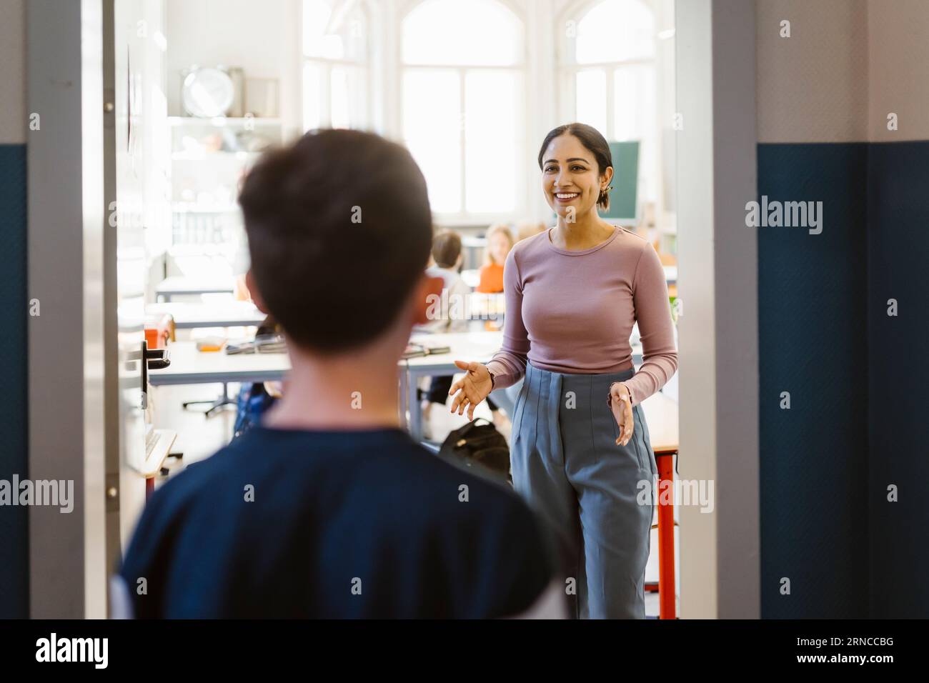 Sorridente insegnante gestante mentre parla con un ragazzo che si trova fuori dall'aula Foto Stock
