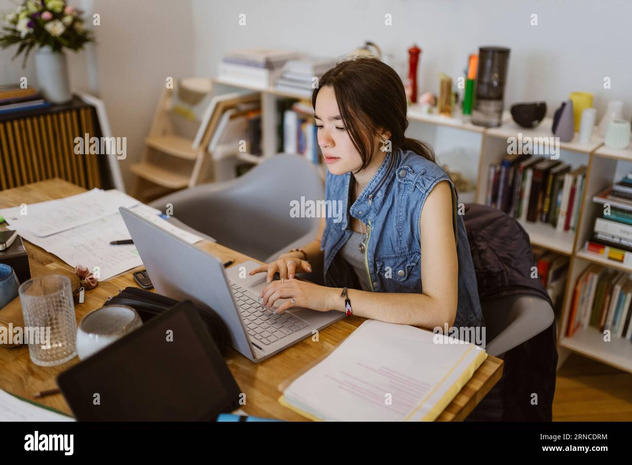 Giovane donna che usa un notebook mentre fa un compito scolastico a casa Foto Stock