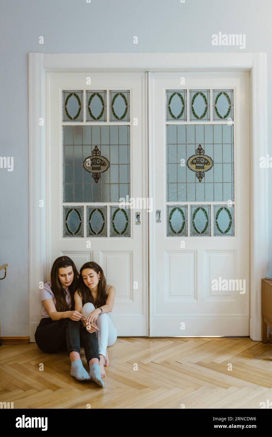 Amici tristi seduti sul pavimento insieme contro la porta bianca a casa Foto Stock