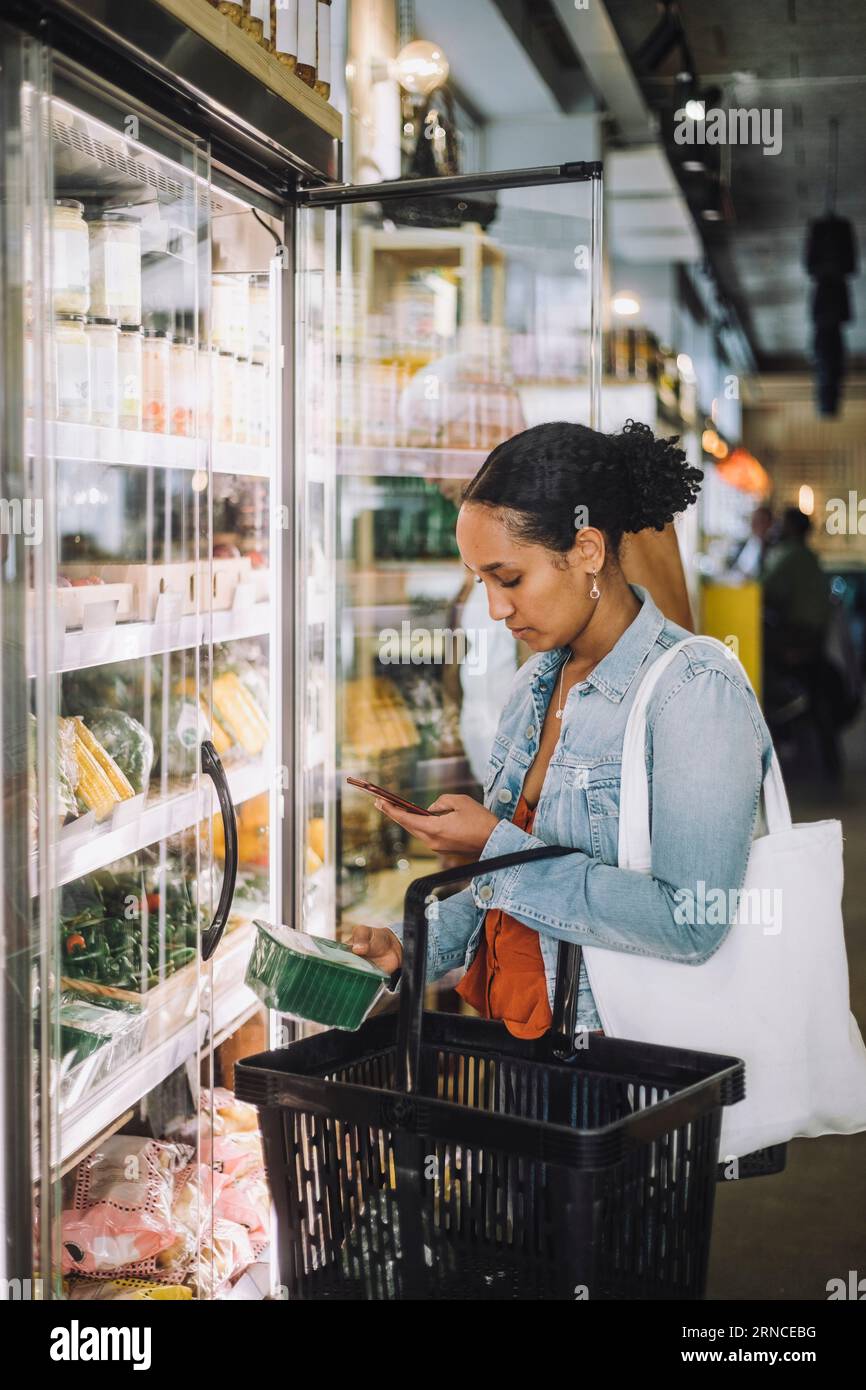 Cliente femminile che fotografa il pacchetto presso la gastronomia biologica Foto Stock