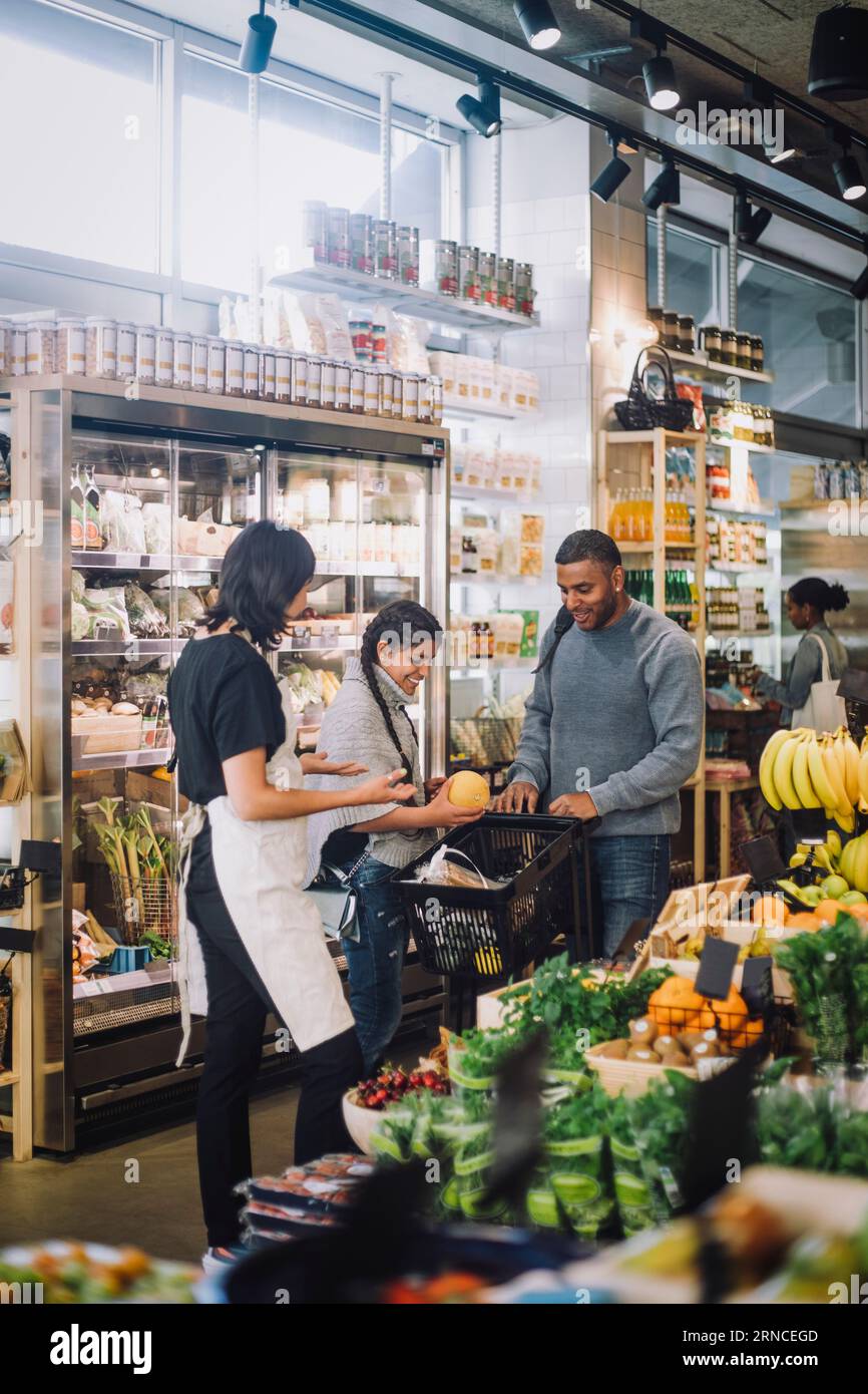 Impiegato di vendita femminile che parla con i clienti che acquistano generi alimentari presso la gastronomia Foto Stock