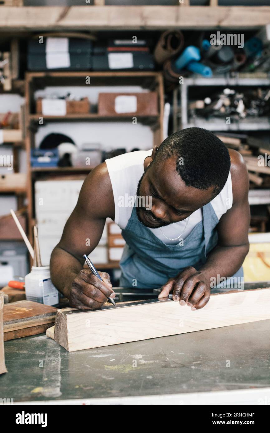 Imprenditore maschio che segna il legno durante l'upcycling in officina Foto Stock