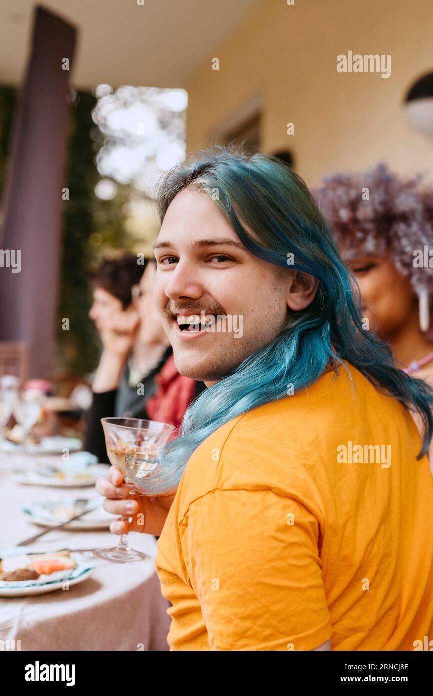 Ritratto di un uomo gay felice con i capelli tinti che si diverte con gli amici durante la cena nel cortile posteriore Foto Stock