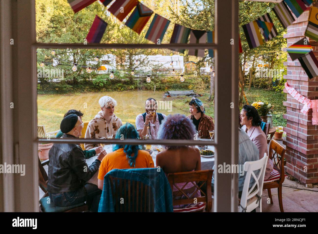 Amici della comunità LGBTQ che si divertono durante la cena nel cortile posteriore visto dalla finestra Foto Stock