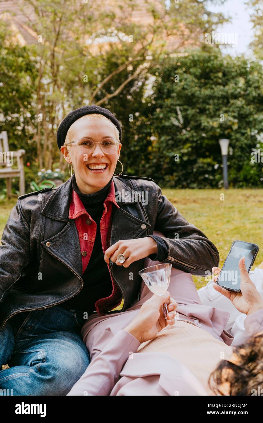 Ritratto di una donna gay felice che indossa una giacca di pelle mentre è seduta con un'amica nel cortile posteriore Foto Stock