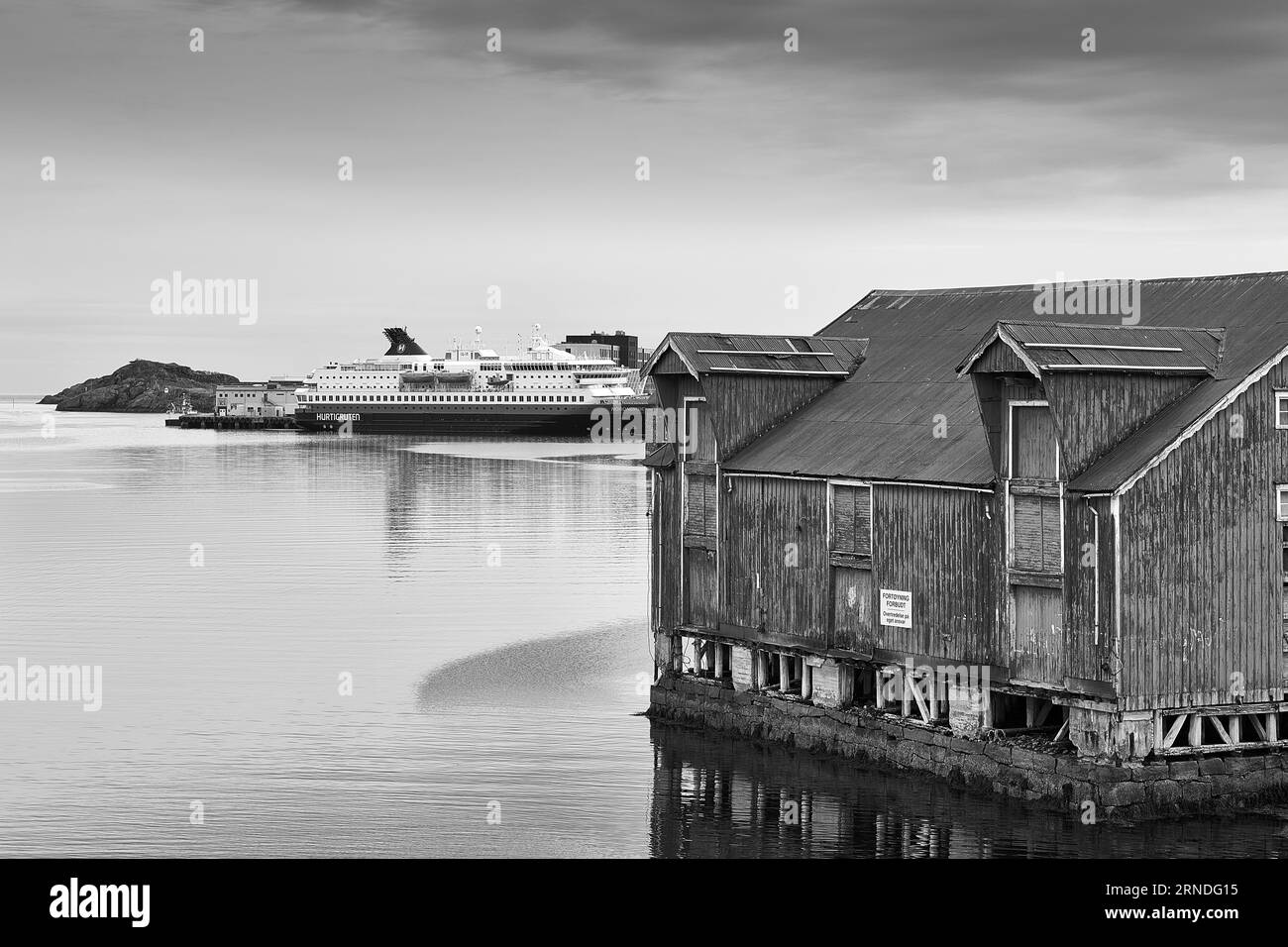 Foto in bianco e nero dei magazzini ittici norvegesi in Foreground e Hurtigruten Ferry, MS NORDNORGE, ormeggiati a Svolvær, nelle isole Lofoten Foto Stock