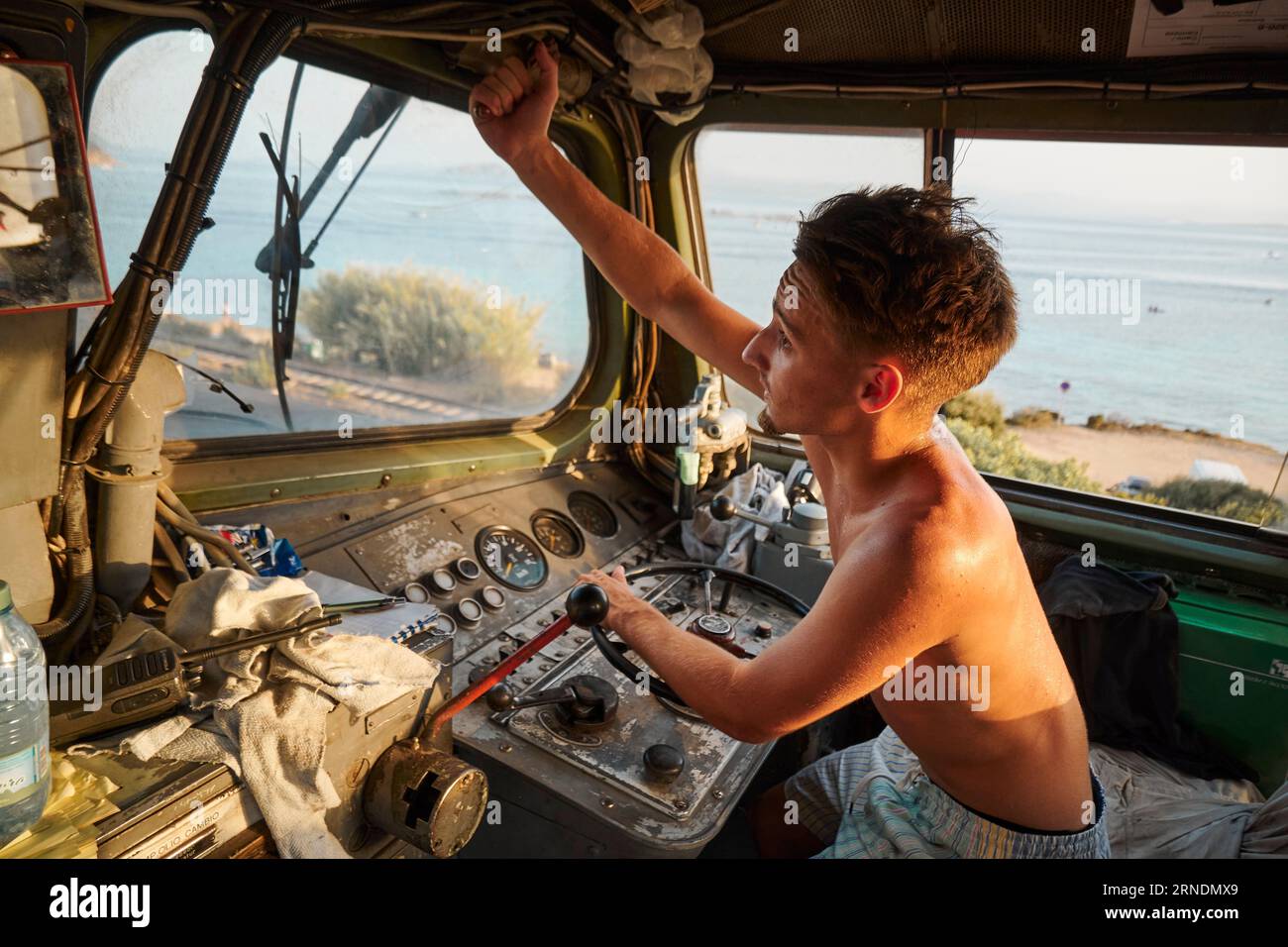 Un uomo caucasico nella cabina di guida di una grande locomotiva, che regola un componente sopra il finestrino Foto Stock