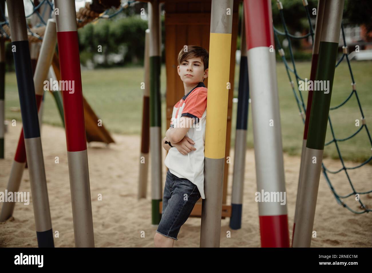 un adolescente con le braccia incrociate si trova accanto al parco giochi pensa a crescere e a pensare di essere vecchio per giocare al parco giochi Foto Stock