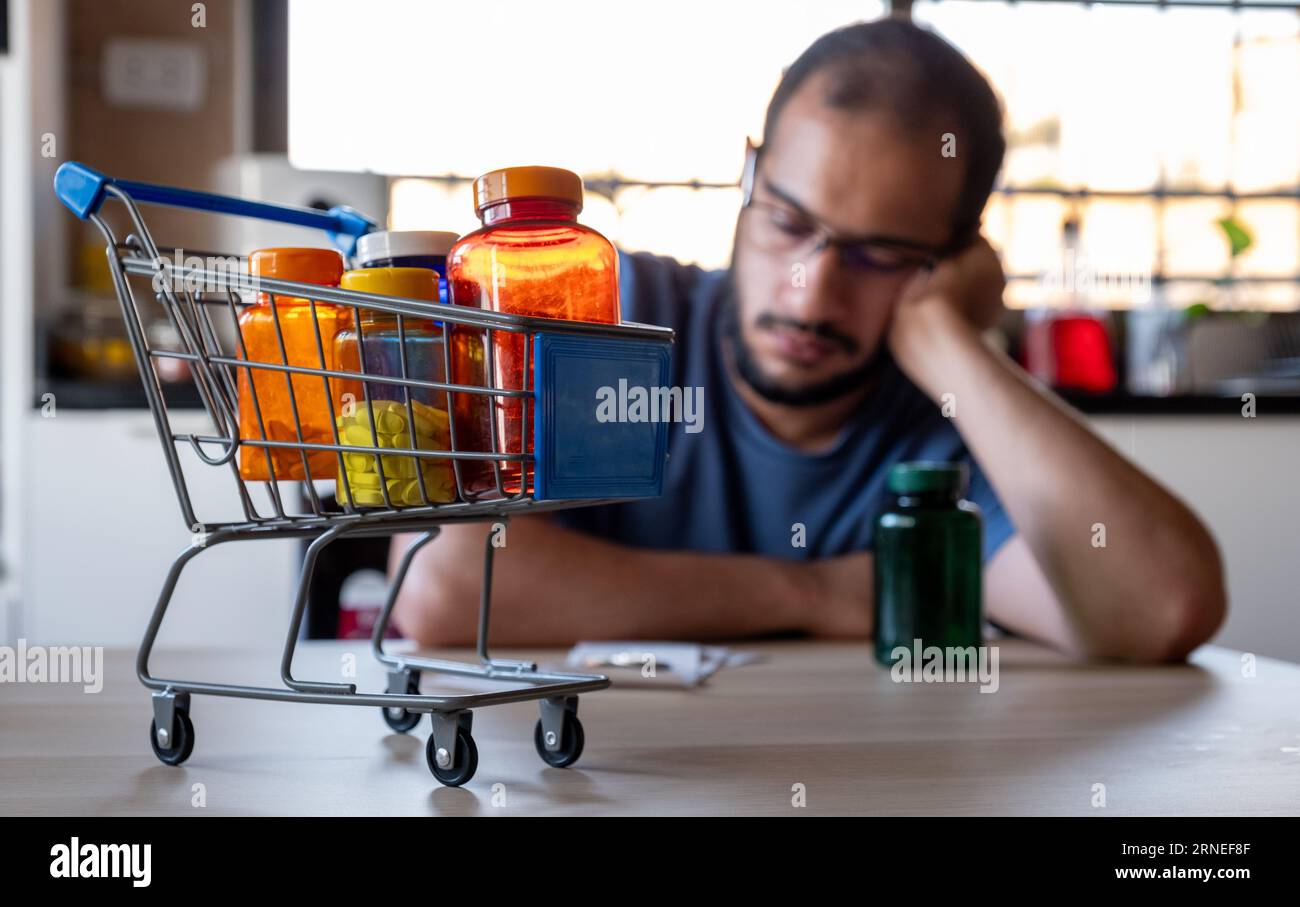 l'uomo seduto in cucina si sentiva frustrato a causa dell'inflazione e dell'aumento delle necessità quotidiane di provviste per la casa con il carrello davanti a sé Foto Stock